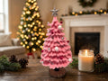 A pink tiered wooden Christmas tree with a silver star topper, decorated with white and red ornaments.